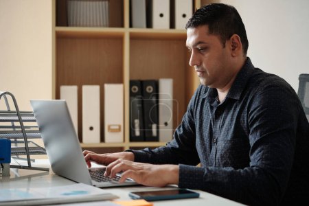 Téléchargez les photos : Homme d'affaires sérieux travaillant sur ordinateur portable à son bureau - en image libre de droit