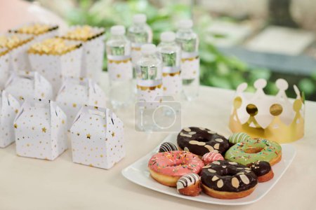 Téléchargez les photos : Assiette avec de délicieux beignets, bouteilles d'eau et boîte avec de petits cadeaux pour les invités de la fête des enfants - en image libre de droit