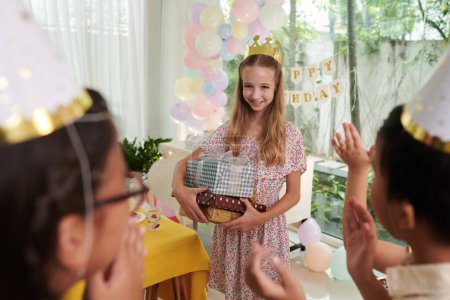 Téléchargez les photos : Sourire fille préadolescente tenant pile de cadeaux d'anniversaire et regardant applaudir des amis - en image libre de droit
