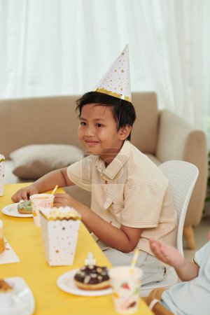Foto de Sonriente preadolescente asiático chico comer dulces en fiesta de cumpleaños - Imagen libre de derechos