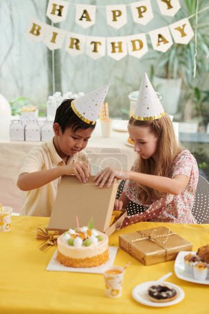 Téléchargez les photos : Curieux enfants ouverture cadeaux à la fête d'anniversaire - en image libre de droit