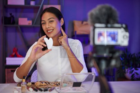 Foto de Sonriente mujer asiática filmando vídeo sobre cómo utilizar gua sha para la mandíbula línea de masaje - Imagen libre de derechos