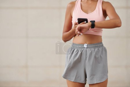 Foto de Imagen recortada de jogger sincronizando la aplicación fitness en su smartwatch y smartphone antes del entrenamiento - Imagen libre de derechos