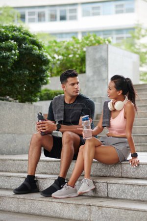 Foto de Ajuste pareja sentada en los escalones, beber agua y hablar después de hacer ejercicio al aire libre - Imagen libre de derechos