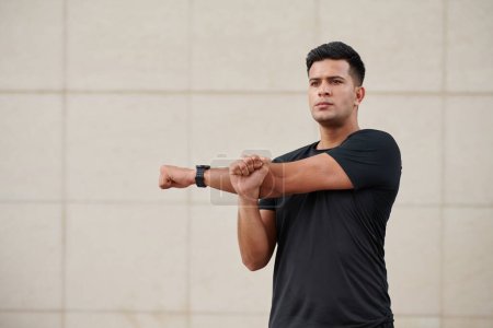 Téléchargez les photos : Portrait d'un sportif déterminé faisant des étirements de bras lors de l'entraînement à l'extérieur - en image libre de droit