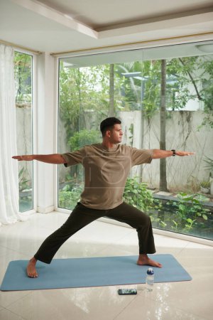 Téléchargez les photos : Fit pieds nus homme pratiquant guerrier yoga pose - en image libre de droit