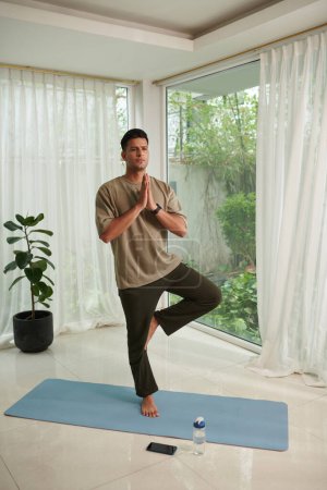 Photo for Fit man keeping hands in namaste gesture when balancing on one foot - Royalty Free Image