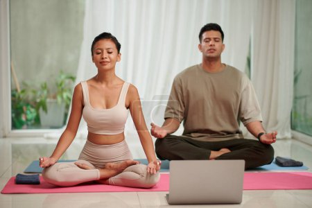 Foto de Novio y novia practicando ejercicios de respiración de yoga, siguiendo tutorial en laptop - Imagen libre de derechos