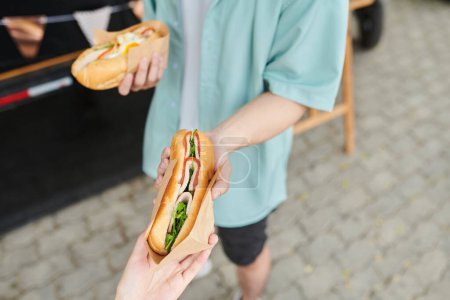 Photo for Hands of young man giving traditional Vietnamese bread called banh mi with ham and vegetables - Royalty Free Image