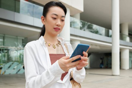Téléchargez les photos : Femme d'affaires joyeuse lisant les messages texte de son collègue lorsqu'elle se tient à l'extérieur - en image libre de droit