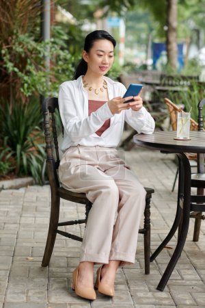 Téléchargez les photos : Portrait de sourire élégante femme d'affaires assis chapeau table de café, ayant boisson rafraîchissante et texto collègue - en image libre de droit