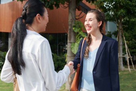 Photo for Excited young female entrepreneur shaking hand of business partner when meeting outdoors - Royalty Free Image