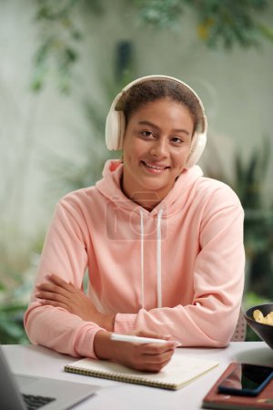 Téléchargez les photos : Portrait d'un étudiant souriant dans un casque écoutant de la musique pendant ses devoirs - en image libre de droit