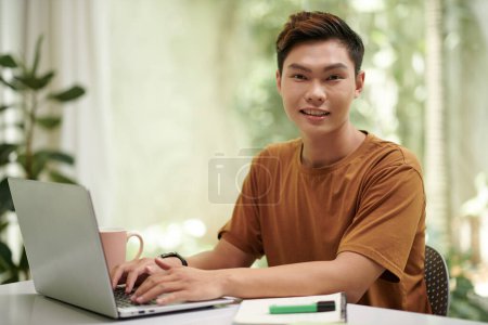 Téléchargez les photos : Joyeux asiatique programmation étudiante en informatique dans un ordinateur portable à la maison - en image libre de droit