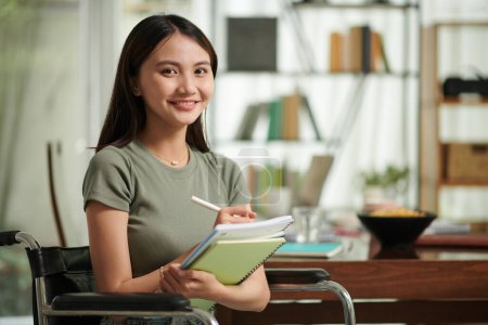 Photo for Portrait of cheerful college student with disability writing in textbook - Royalty Free Image