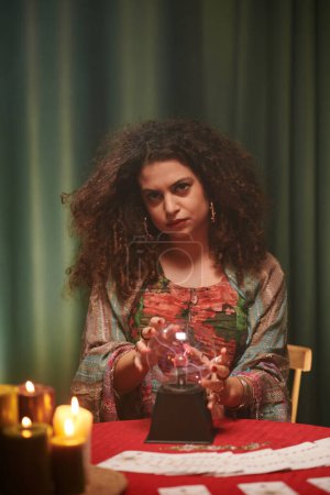 Téléchargez les photos : Portrait d'une sorcière sérieuse utilisant une boule de cristal pour voir la fortune du client - en image libre de droit