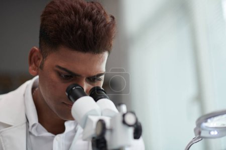 Téléchargez les photos : Ingénieur indien sérieux regardant au microscope - en image libre de droit