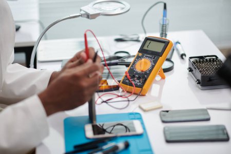 Photo for Engineer using multimeter when examining if smartphone works good after repairing - Royalty Free Image