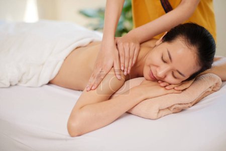 Téléchargez les photos : Masseur professionnel massant dos de jeune femme asiatique dans le salon de spa - en image libre de droit