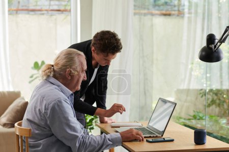 Foto de Adolescente chico mostrando abuelo cómo utilizar el ordenador portátil - Imagen libre de derechos