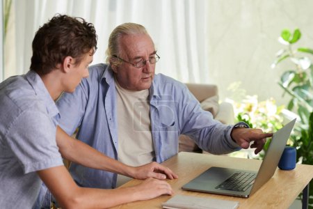 Photo for Senior man asking grandson to help him with installing applications on laptop - Royalty Free Image