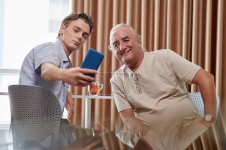 Photo for Young man taking selfie with smiling grandfather - Royalty Free Image