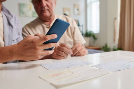 Foto de Imagen de primer plano del joven que muestra al abuelo cómo pagar facturas en línea a través de la aplicación móvil - Imagen libre de derechos