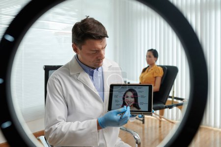 Téléchargez les photos : Médecin pointant vers le graphique sur tablette expliquant comment beaucoup de traitement des rides dont vous avez besoin - en image libre de droit