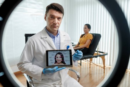 Foto de Retrato del cosmetólogo apuntando a la carta de tableta digital al explicar a los suscriptores cuánto tratamiento de belleza para obtener - Imagen libre de derechos