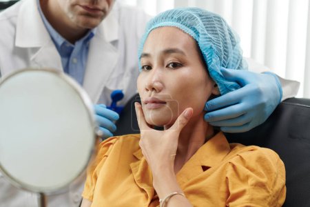 Téléchargez les photos : Jeune femme touchant son visage après avoir reçu un traitement de beauté dans une clinique médicale - en image libre de droit
