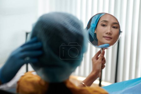 Photo for Young Asian woman looking at mirror after getting beauty treatment in clinic - Royalty Free Image
