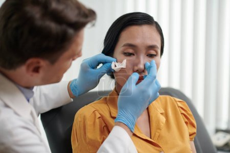 Téléchargez les photos : Chirurgien plastique examinant le nez du patient après rhinoplastie - en image libre de droit