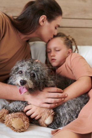 Photo for Mother kissing daughter fell asleep hugging her small dog - Royalty Free Image