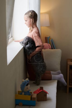 Photo for Curious girl and her best friend dog hugging and looking outside through window - Royalty Free Image