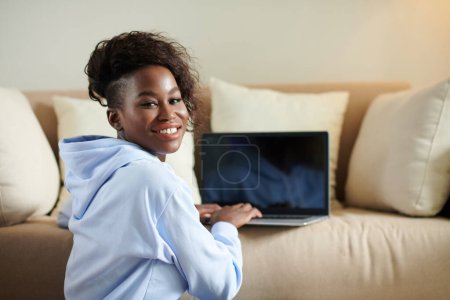 Foto de Retrato de una joven negra sonriente trabajando en un portátil y volviendo a la cámara - Imagen libre de derechos