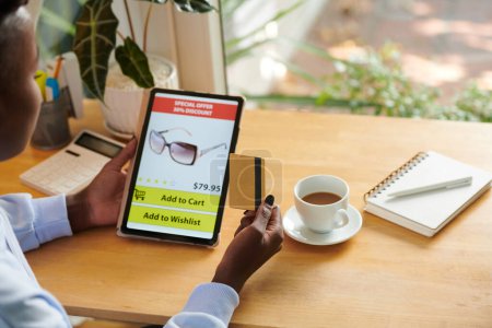Téléchargez les photos : Jeune femme faisant du shopping en ligne via application sur tablette et commande de lunettes de soleil - en image libre de droit