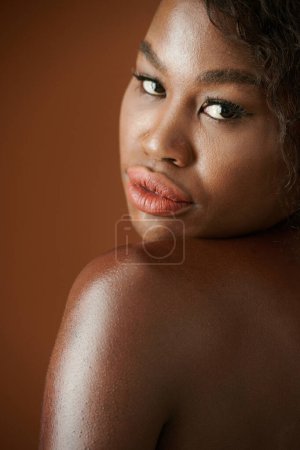 Téléchargez les photos : Sérieux sensuel nu jeune femme noire regardant par-dessus l'épaule - en image libre de droit