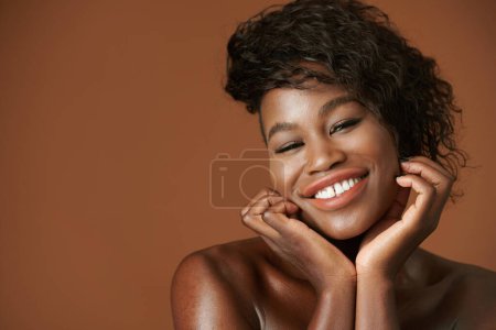 Téléchargez les photos : Portrait de charmante jeune femme noire souriante aux cheveux bouclés regardant la caméra - en image libre de droit