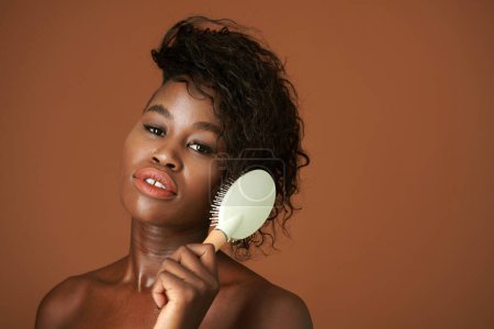 Téléchargez les photos : Studio portrait de jeune femme noire brossant les cheveux après la douche du matin - en image libre de droit