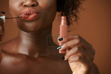 Photo for Cropped image of Black young woman applying matte liquid lipstick when doing makeup in the morning - Royalty Free Image