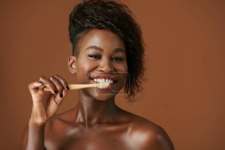 Foto de Emocionado joven mujer negra cepillarse los dientes con pasta de dientes blanqueador por la mañana - Imagen libre de derechos