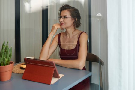Téléchargez les photos : Portrait de femme d'affaires elelegant positif assis au bureau dans son bureau à la maison lorsque vous travaillez sur tablette - en image libre de droit