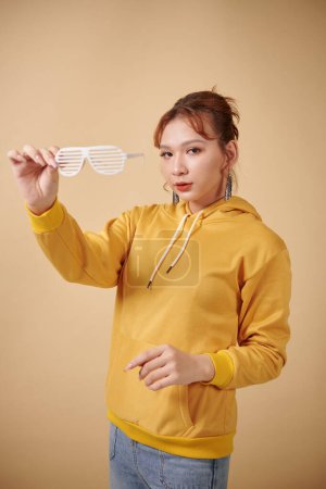 Téléchargez les photos : Femme transgenre à capuche jaune posant avec des lunettes en plastique - en image libre de droit
