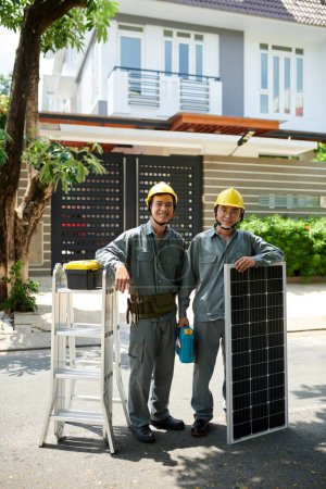 Foto de Contratistas vietnamitas positivos de pie en la casa del cliente listos para instalar paneles solares - Imagen libre de derechos