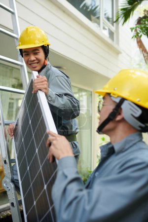 Photo for Contractors lifting solar panel on house roof - Royalty Free Image
