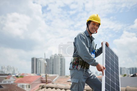 Photo for Positive Vietnamese contractor standing on roof with solar panel - Royalty Free Image