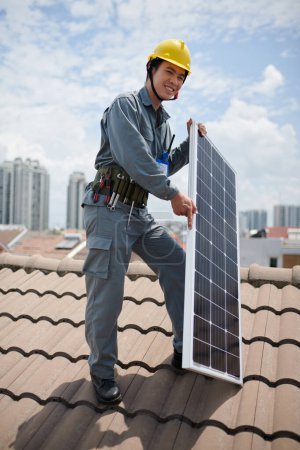 Téléchargez les photos : Bâtisseur joyeux debout sur le toit avec panneau photovoltaïque - en image libre de droit