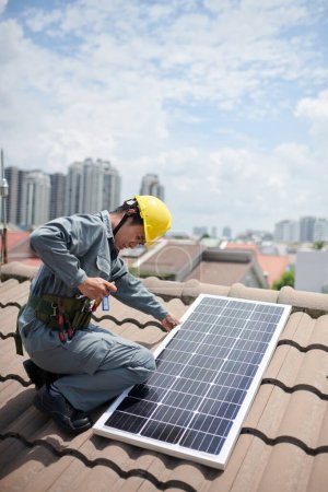 Photo for Contractor taking tools out of pocket when installing solar panel on roof - Royalty Free Image