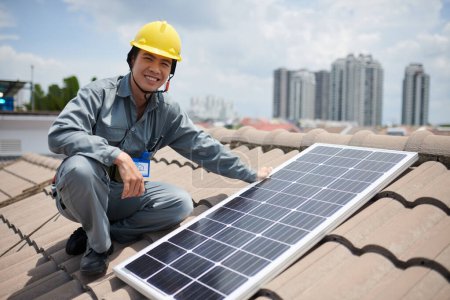 Photo for Positive Asian contractor installing solar panel on tile roof - Royalty Free Image