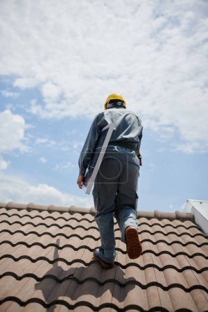 Photo for Engineer carrying solar panel when walking on roof, view from back - Royalty Free Image